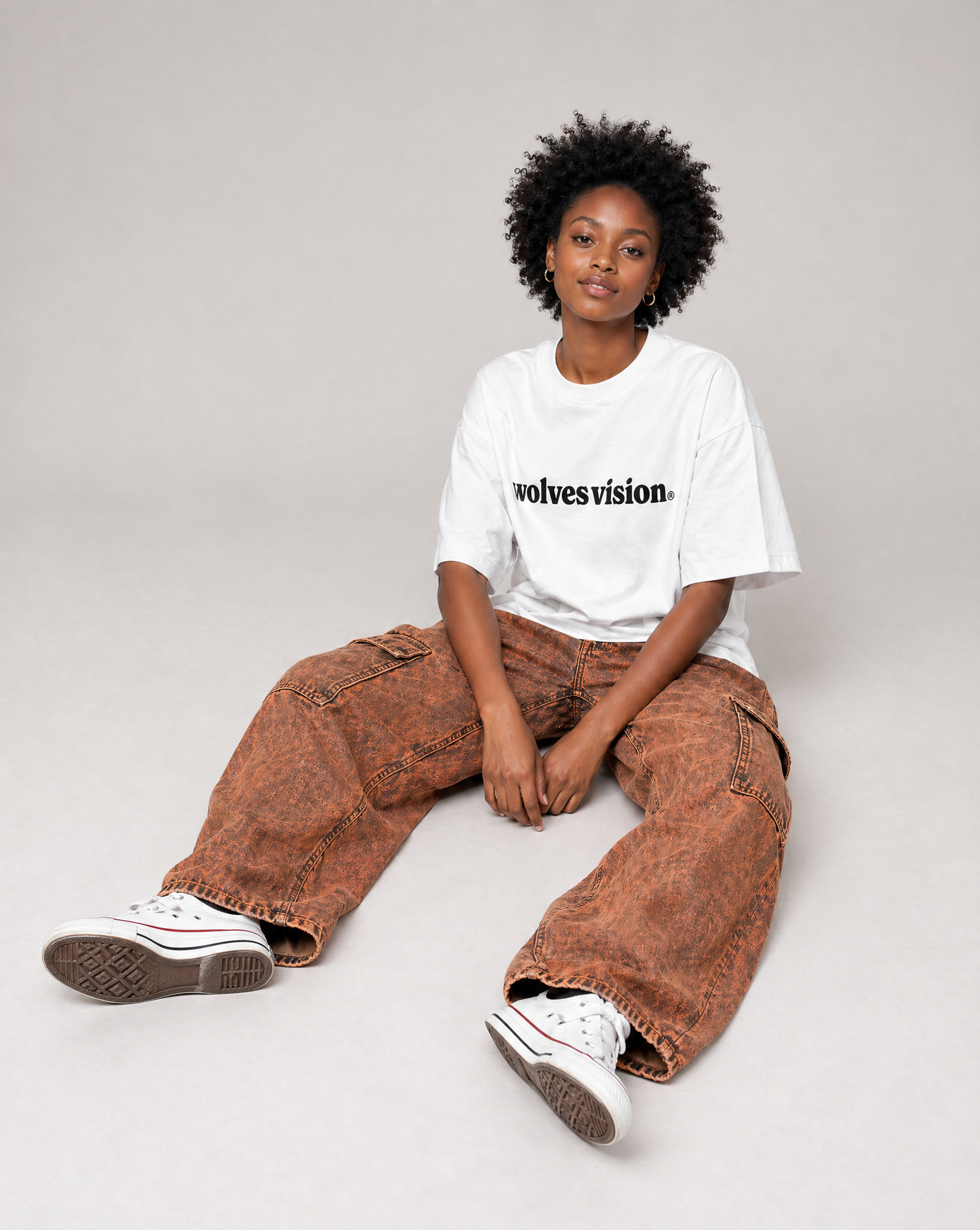 Person wearing a white t-shirt with text saying "wolves vision®" and brown pants sitting on a light gray background