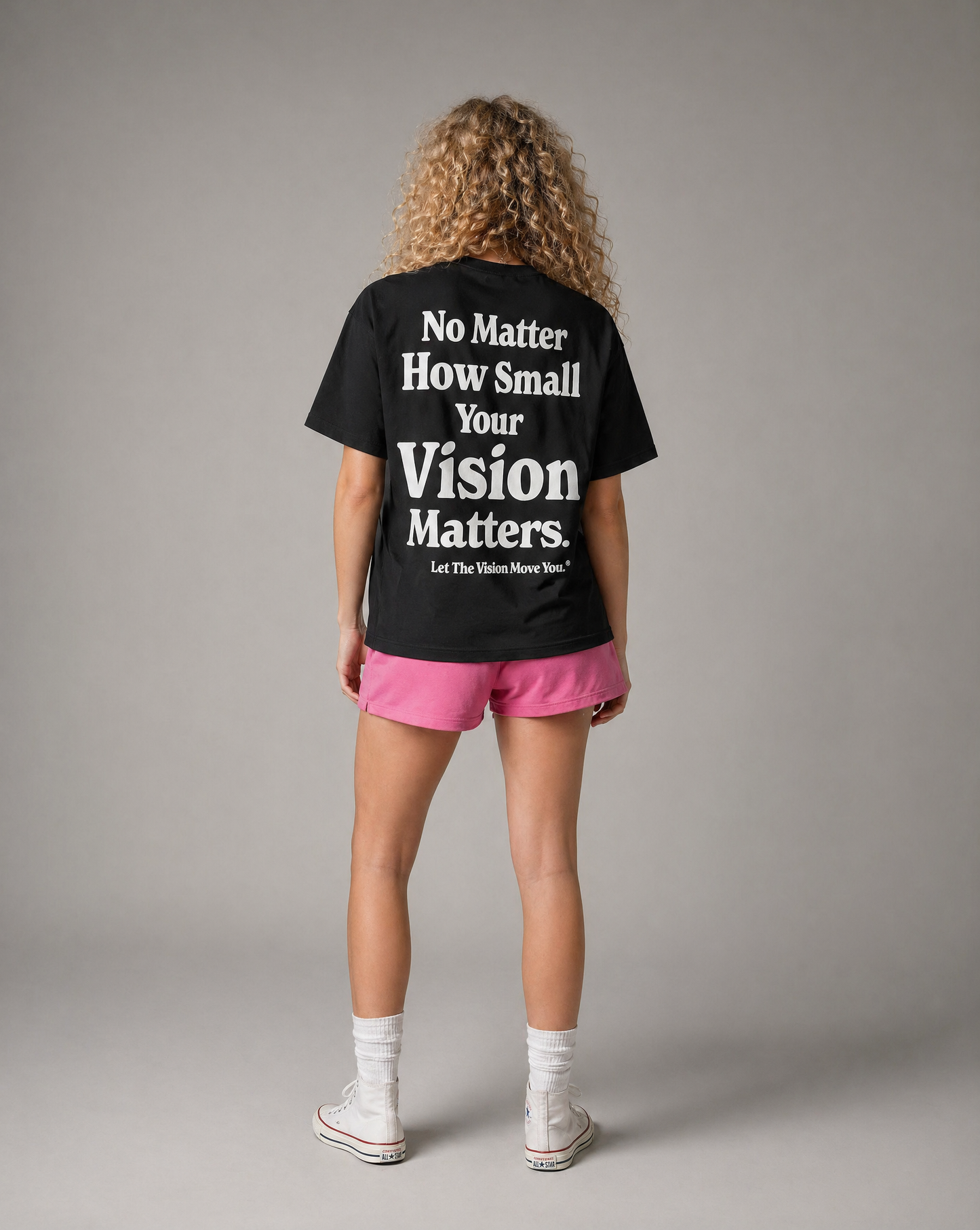Person wearing a black t-shirt with motivational quote on the back, standing against a gray background
