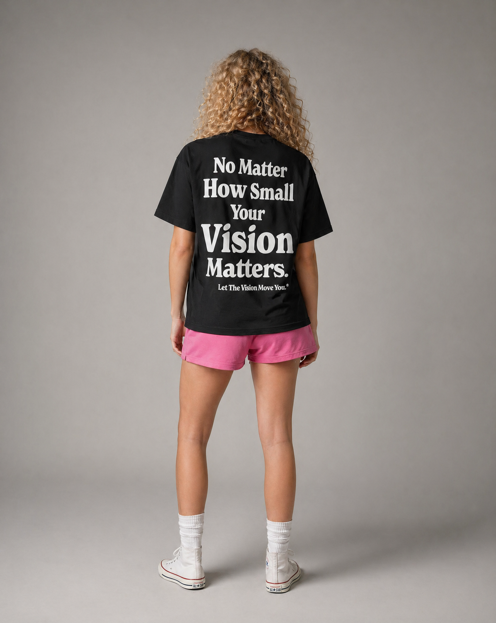 Person wearing a black t-shirt with motivational quote on the back, standing against a gray background