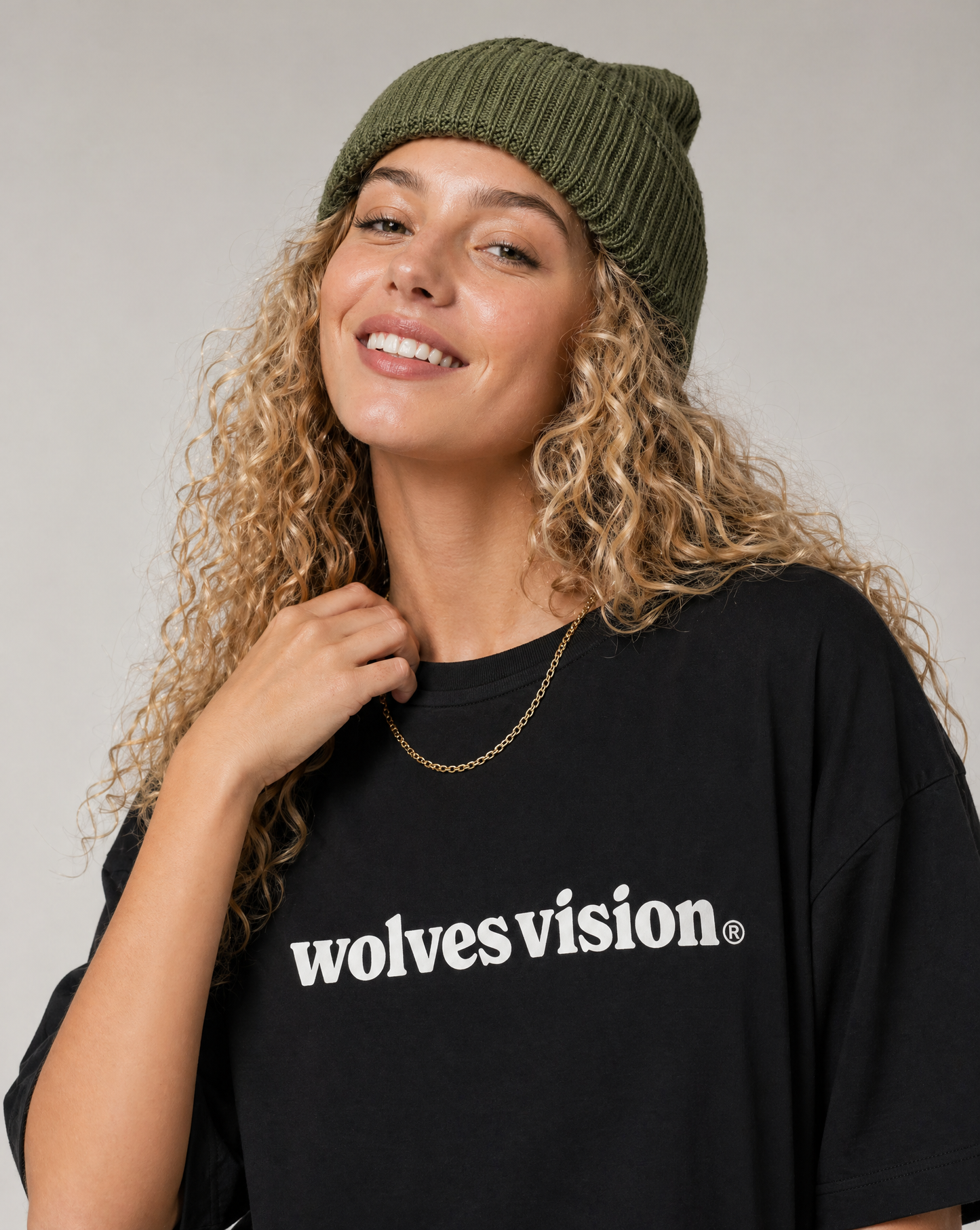 Woman wearing a black 'wolvesvision' t-shirt with a green beanie against a plain background